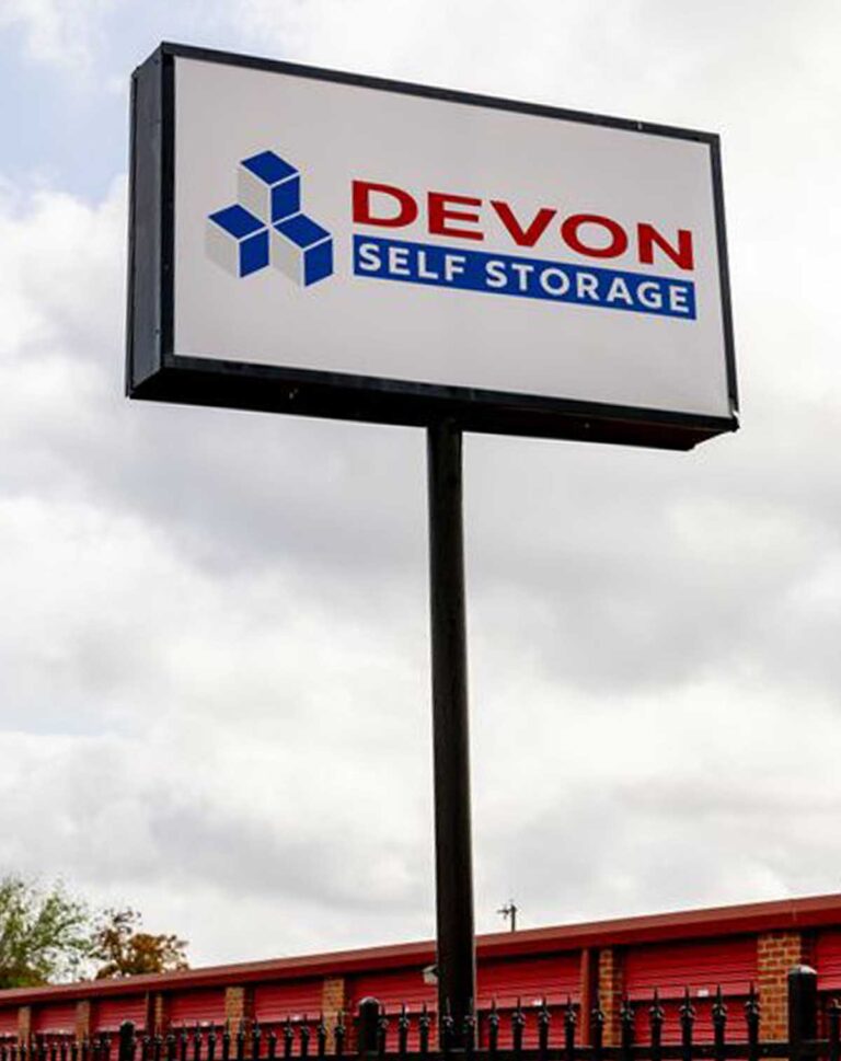 Devon Self Storage pole sign with blue geometric logo and red lettering